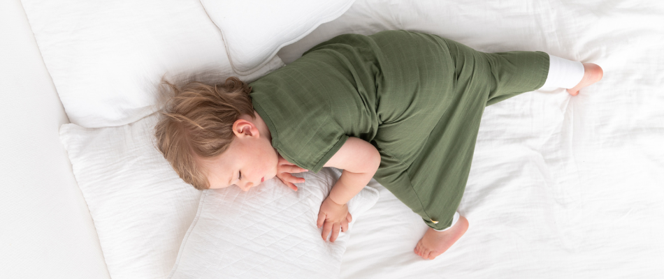 baby sleeping on bed in green sleeping bag with feet