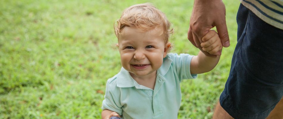 toddler boy holding dad's hand in park